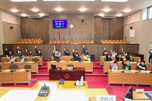 議員席で手を挙げる児童たち